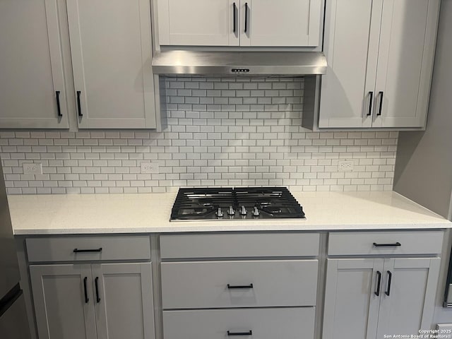 kitchen with under cabinet range hood, stainless steel gas cooktop, gray cabinets, and backsplash