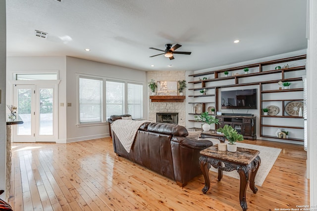 living room featuring light wood finished floors, visible vents, a ceiling fan, a stone fireplace, and recessed lighting