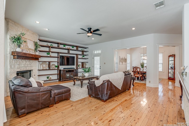 living room with light wood-style floors, visible vents, plenty of natural light, and a stone fireplace