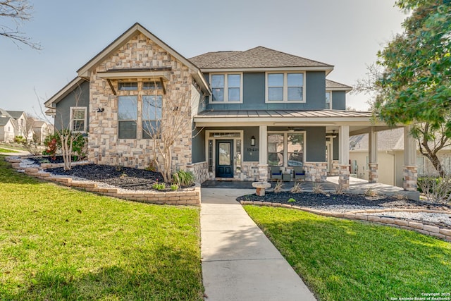 view of front of home featuring metal roof, covered porch, stone siding, a front lawn, and a standing seam roof