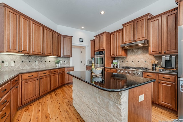 kitchen with appliances with stainless steel finishes, light wood-type flooring, brown cabinets, and under cabinet range hood