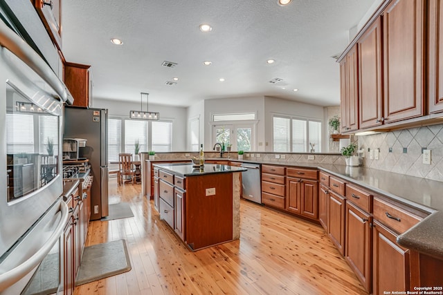 kitchen with visible vents, appliances with stainless steel finishes, light wood-type flooring, backsplash, and brown cabinets