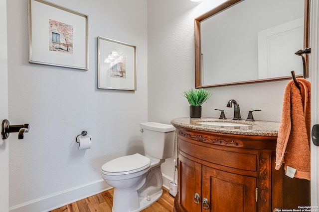 half bathroom featuring toilet, baseboards, wood finished floors, and vanity