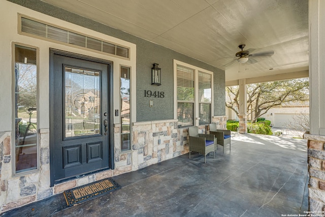 entrance to property featuring ceiling fan, stone siding, and stucco siding