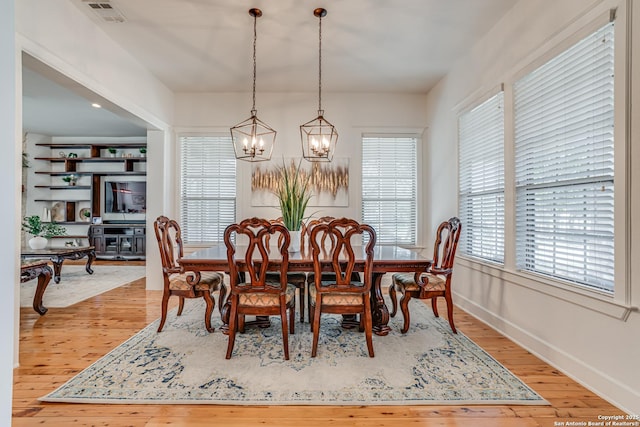 dining room featuring light wood finished floors, an inviting chandelier, visible vents, and baseboards