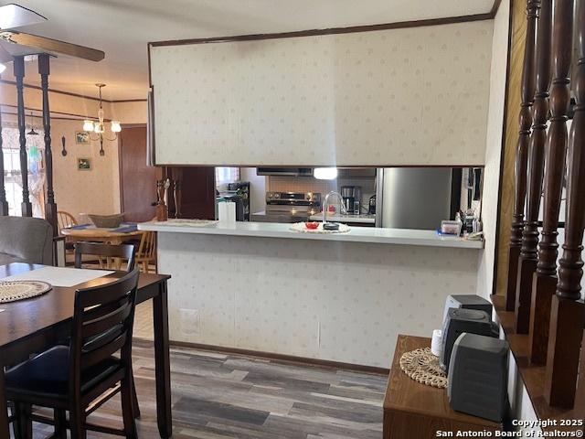 kitchen with a notable chandelier, stainless steel appliances, a peninsula, wood finished floors, and wallpapered walls