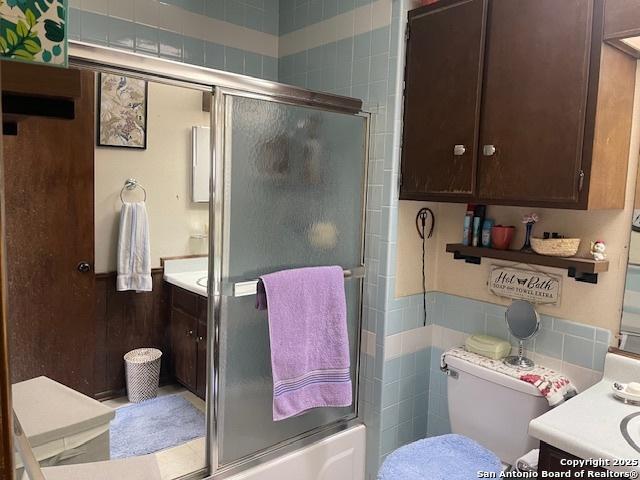 bathroom with toilet, shower / bath combination with glass door, tile walls, and vanity