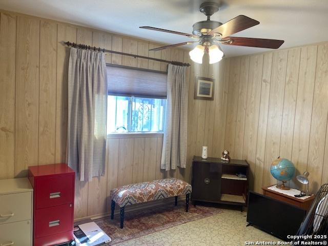 living area featuring a ceiling fan and wooden walls