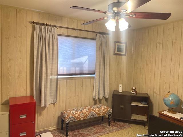 sitting room featuring wooden walls and a ceiling fan