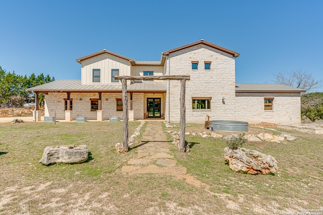 back of property with metal roof, stone siding, a standing seam roof, and a lawn