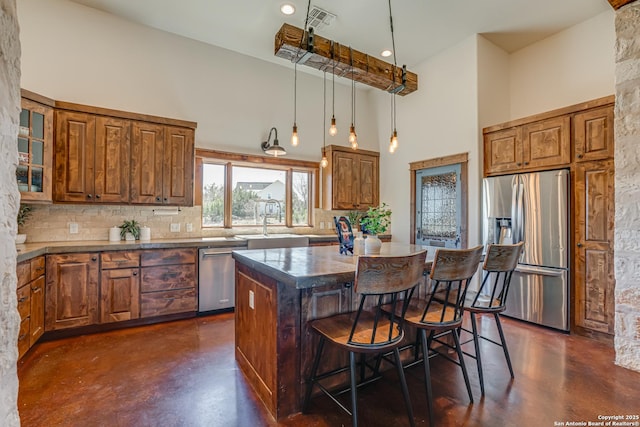 kitchen featuring a towering ceiling, appliances with stainless steel finishes, a kitchen breakfast bar, a center island, and finished concrete floors