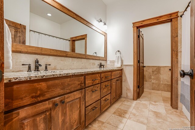 bathroom featuring a wainscoted wall, a sink, tile walls, and double vanity