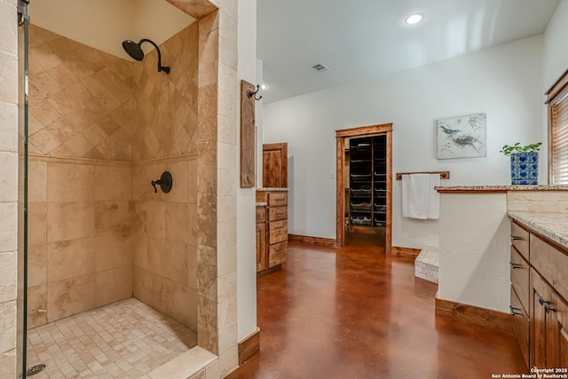 bathroom with finished concrete flooring, baseboards, visible vents, a tile shower, and vanity