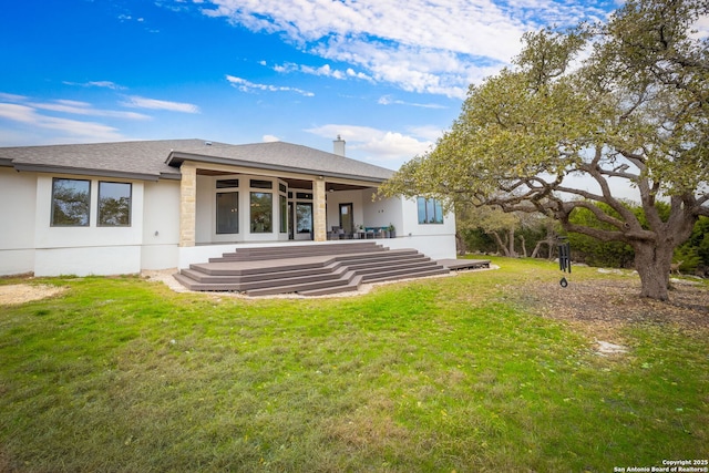 back of property featuring a shingled roof, a lawn, and stucco siding