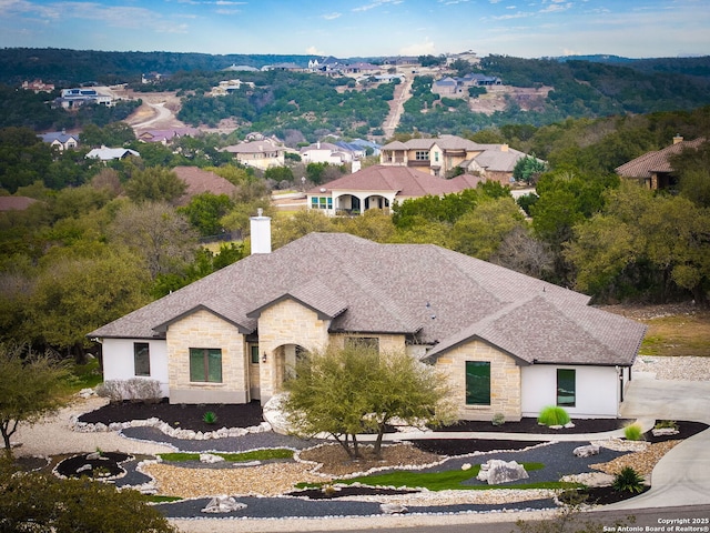 view of front of home with stone siding, roof with shingles, and a chimney