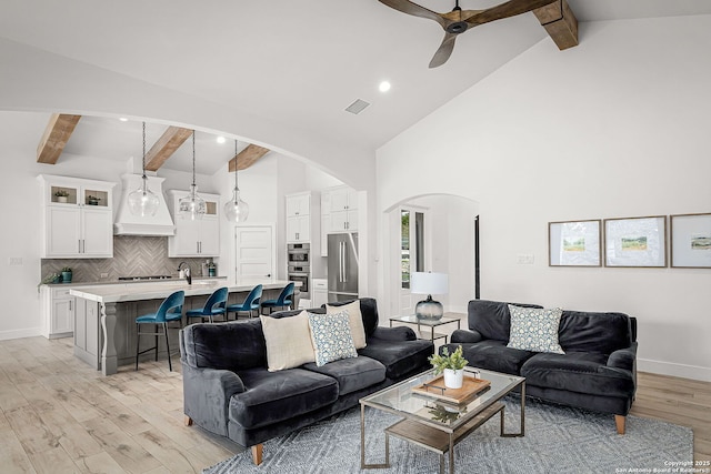 living room featuring visible vents, arched walkways, baseboards, light wood-style floors, and high vaulted ceiling