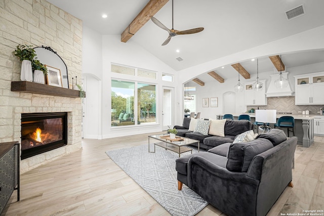 living area with arched walkways, light wood-style flooring, a fireplace, visible vents, and beam ceiling