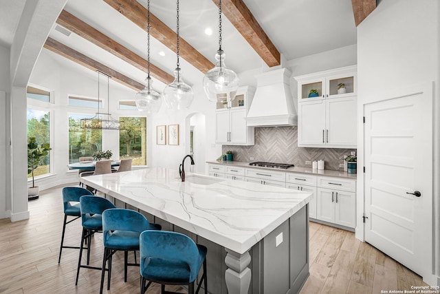 kitchen featuring arched walkways, custom exhaust hood, tasteful backsplash, a sink, and an island with sink