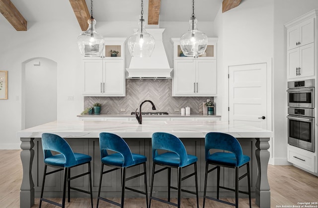 kitchen with double oven, light wood finished floors, light stone counters, and white cabinetry