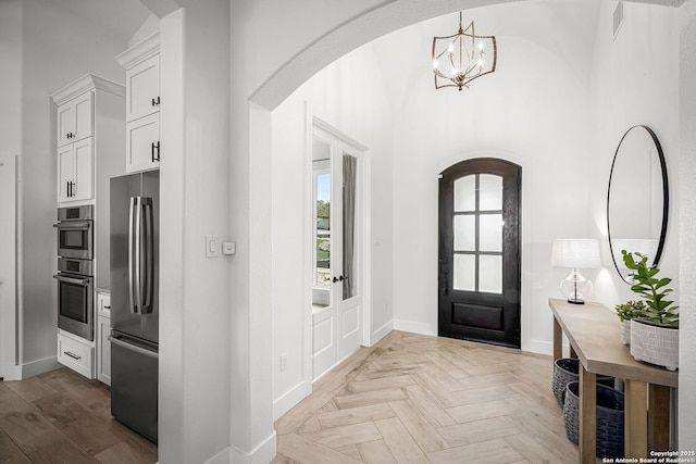 foyer with arched walkways, a chandelier, a towering ceiling, visible vents, and baseboards