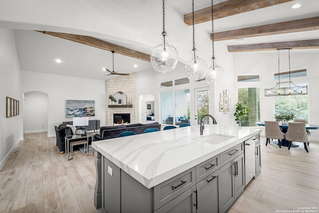 kitchen featuring arched walkways, light wood-style flooring, gray cabinetry, a fireplace, and a sink