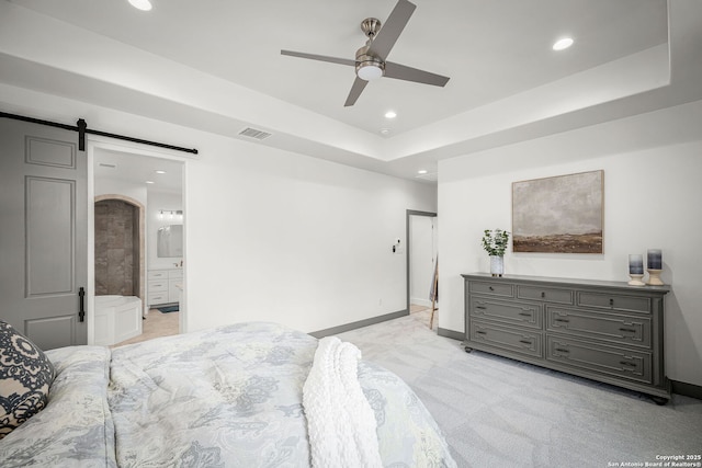 bedroom with a tray ceiling, recessed lighting, visible vents, a barn door, and baseboards