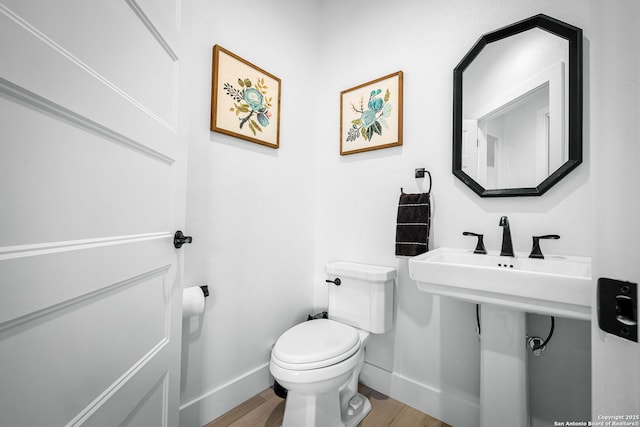 bathroom with toilet, a sink, baseboards, and wood finished floors