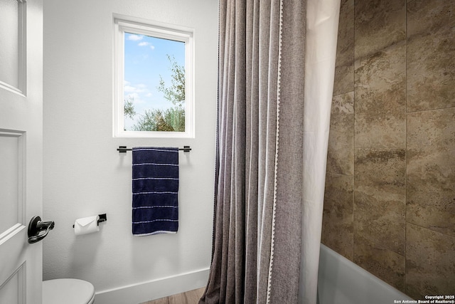 bathroom featuring toilet, baseboards, and shower / tub combo with curtain