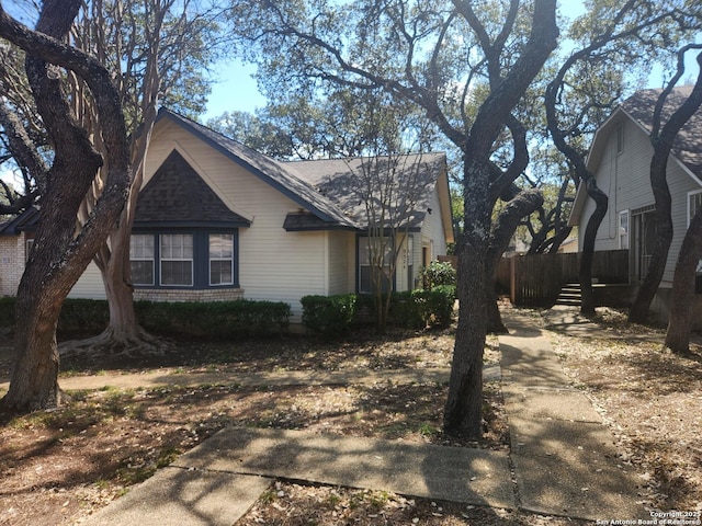 view of side of home featuring a shingled roof, fence, and brick siding