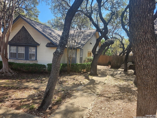 view of front of property with brick siding, fence, and roof with shingles