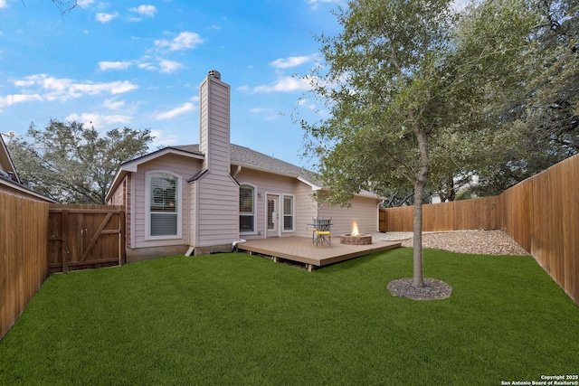 rear view of house featuring a fenced backyard, a chimney, a deck, and a yard