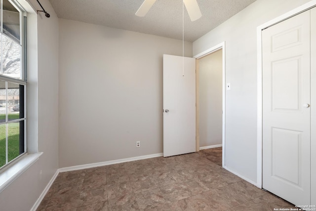 unfurnished bedroom featuring ceiling fan, a textured ceiling, and baseboards