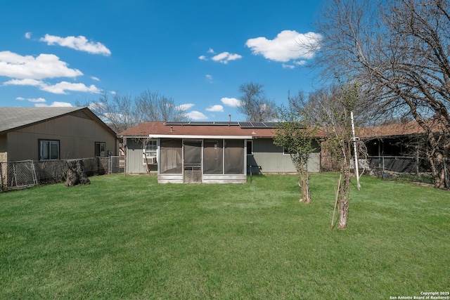 rear view of house with a sunroom, a fenced backyard, a lawn, and solar panels