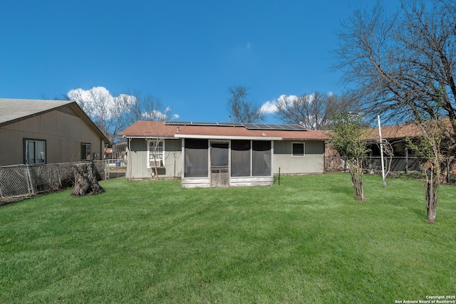 rear view of property featuring a lawn, a fenced backyard, a sunroom, and roof mounted solar panels