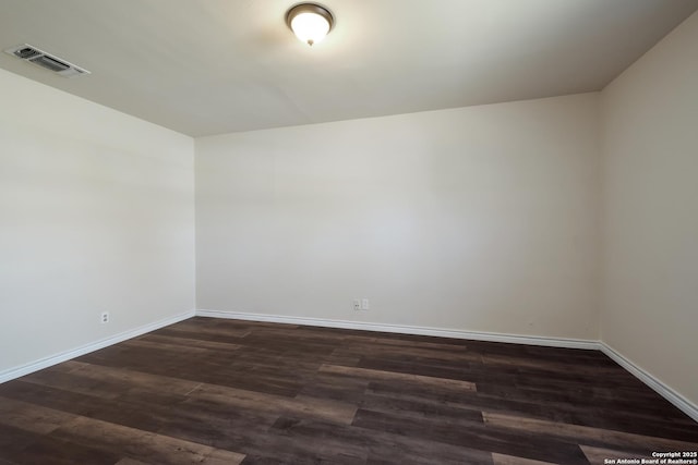 empty room with baseboards, visible vents, and dark wood-type flooring