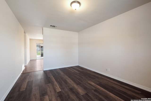 empty room with baseboards, visible vents, and dark wood-style flooring