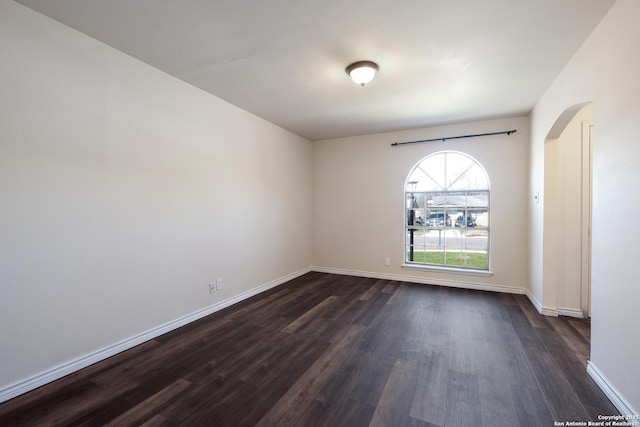 unfurnished room with arched walkways, dark wood-style flooring, and baseboards