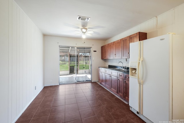 kitchen featuring white refrigerator with ice dispenser, visible vents, a ceiling fan, dark tile patterned floors, and a sink