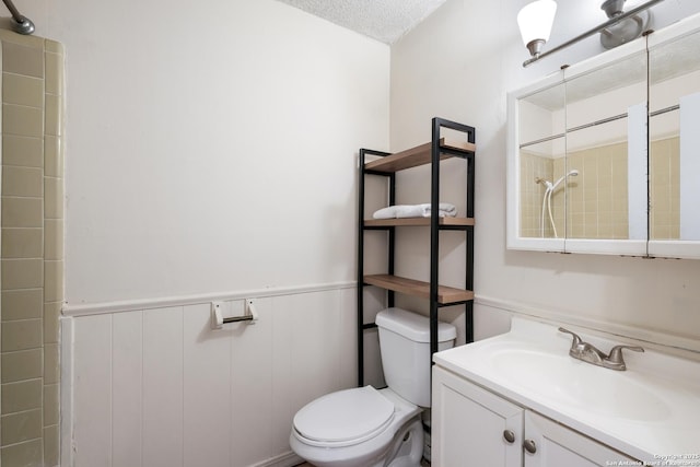 bathroom with a shower, wainscoting, vanity, and toilet