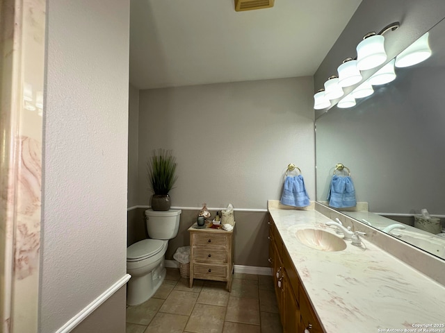 half bathroom with toilet, baseboards, vanity, and tile patterned floors