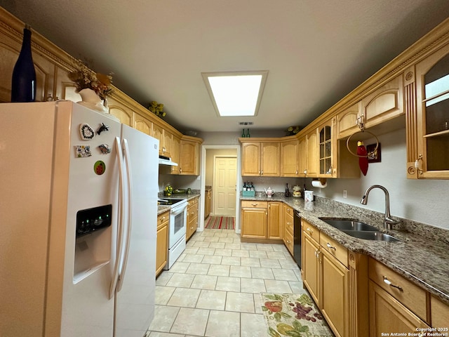 kitchen featuring white appliances, glass insert cabinets, dark stone countertops, under cabinet range hood, and a sink