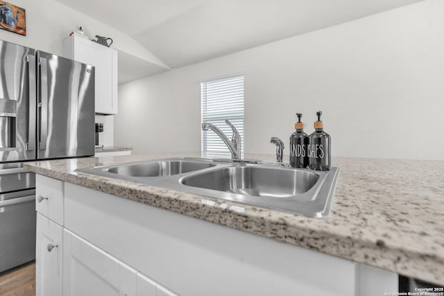 kitchen featuring vaulted ceiling, a sink, white cabinets, and stainless steel fridge with ice dispenser