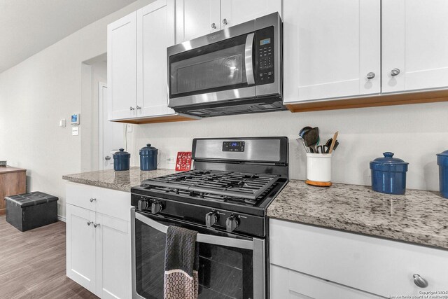 kitchen featuring stainless steel appliances, light stone countertops, light wood-style flooring, and white cabinets