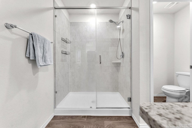 bathroom featuring a stall shower, wood finished floors, toilet, and baseboards