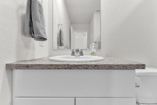 bathroom with vanity, visible vents, and a textured wall