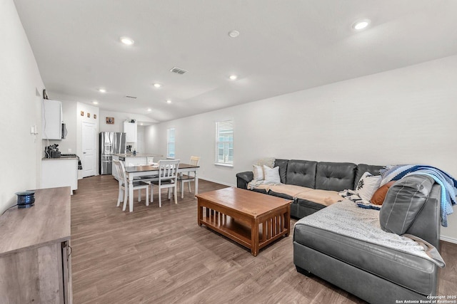 living room with light wood-type flooring, visible vents, vaulted ceiling, and recessed lighting