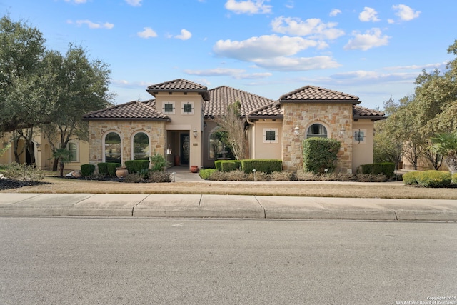 mediterranean / spanish house featuring stone siding, a tile roof, and stucco siding