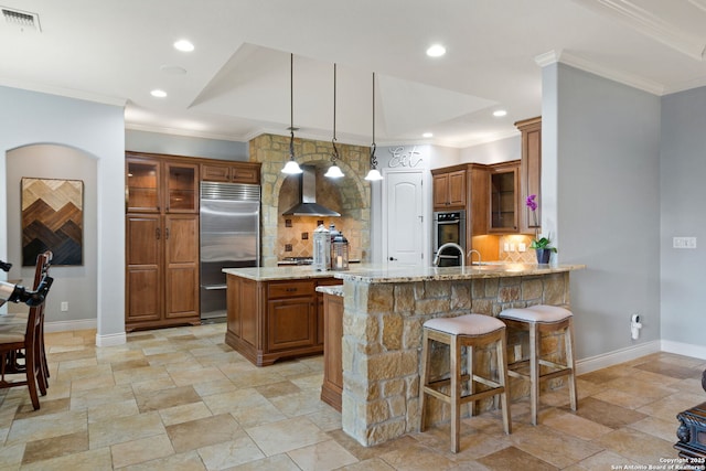 kitchen with wall chimney exhaust hood, visible vents, appliances with stainless steel finishes, and brown cabinetry