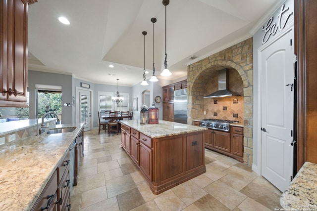 kitchen with appliances with stainless steel finishes, a sink, light stone countertops, wall chimney range hood, and backsplash