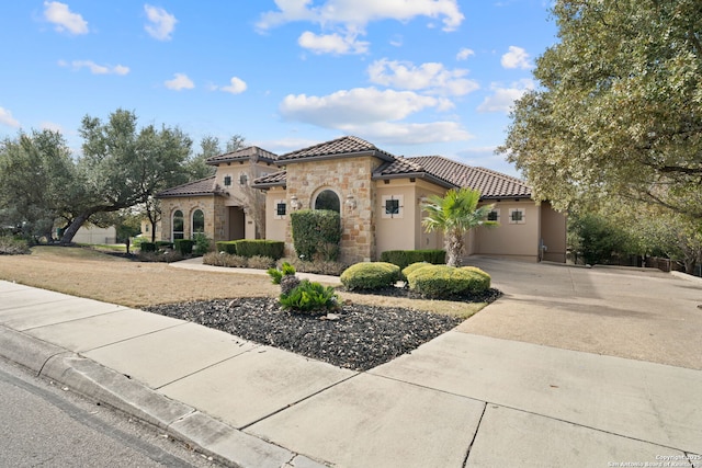 mediterranean / spanish-style home with stone siding, a tiled roof, driveway, and stucco siding